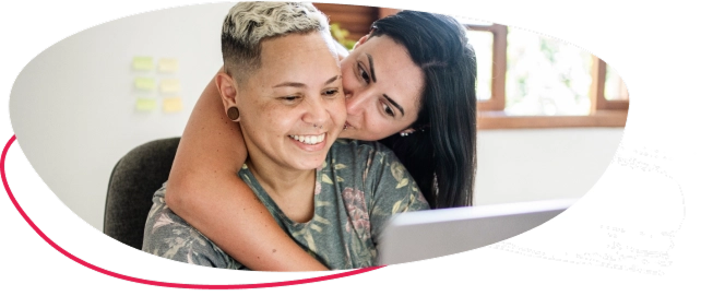 Two women embracing sitting in front of a laptop embracing